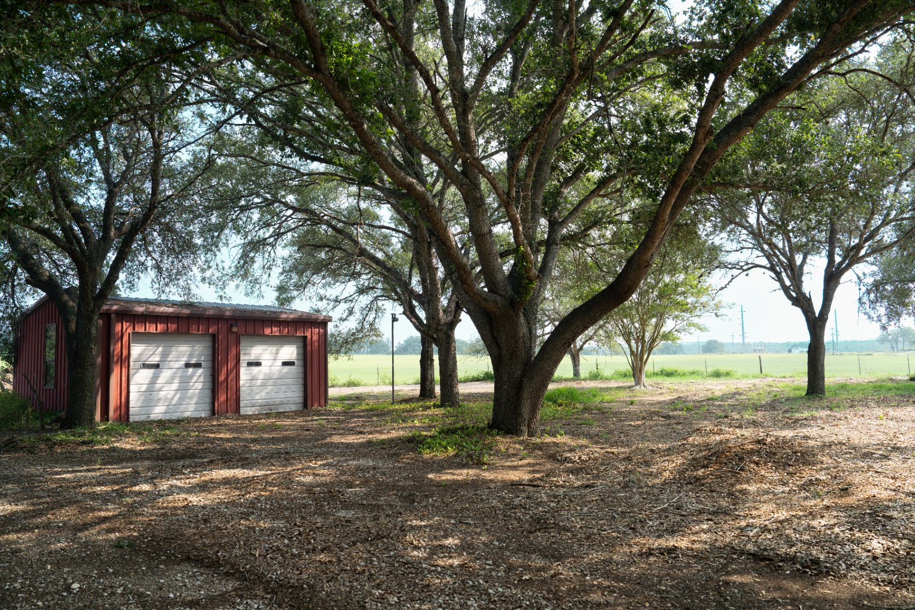 Large red workshop under mature trees behind the home